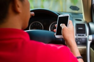 Asian man sitting in car with mobile phone in hand texting while driving