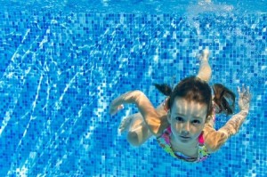 Happy active child swims underwater in pool, beautiful healthy girl swimming and having fun on family summer vacation, kids sport concept