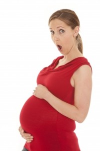 A pregnant woman in a red shirt looks shocked.