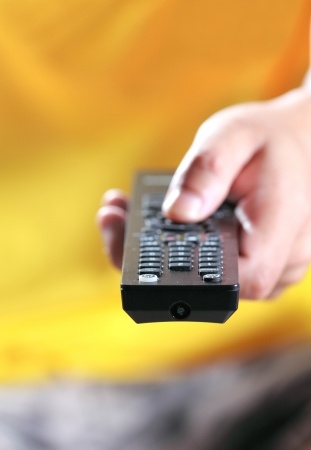 Hand pressing remote control, watching tv on the sofa