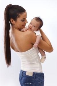 Pretty young mother holding newborn baby in arm, embracing, smiling happy.