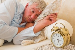 Sleepy elderly man waking up and looking at the alarm clock with one eye - focus is on the alarm clock