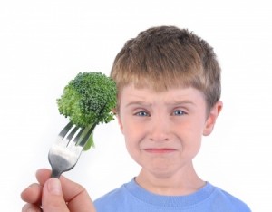 A young boy is making a funny disgusting face at a fork with a healthy piece of broccoli on a white background.