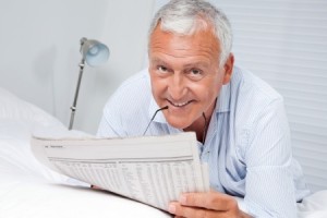 Portrait of senior man reading newspaper lying on bed at home