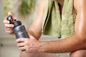 Tired man resting after training, holding bottle in hand. Selective focus on bottle.