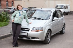 Happy woman standing in front of own new car