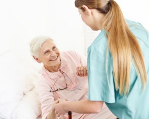 Nurse at extended home care helping smiling senior woman out of bed