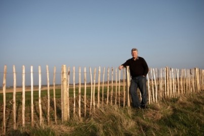 A mature man standing against a fence with hand in pocket