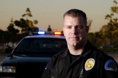 A serious looking police officer standing in front of his patrol car
