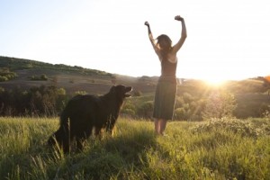 Beautiful woman raises her arms to the sun in joy whilst walking her dog