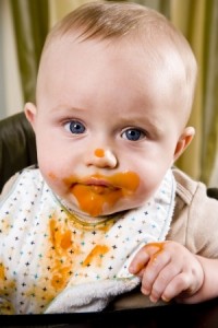 Messy six month old baby wearing bib after eating solid food