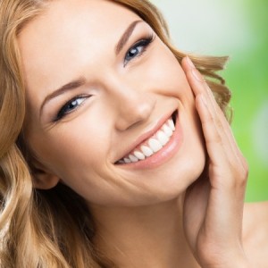 Portrait of happy smiling beautiful young woman touching skin or applying cream, outdoors