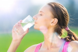 Portrait of young beautiful dark-haired woman wearing pink t-shirt drinking water after sport exercise at summer green park