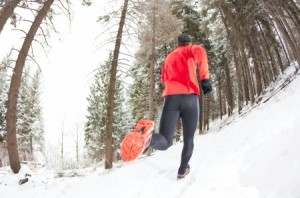 Winter trail running man takes a run on a snowy mountain path in a pine woods