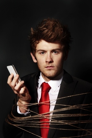 low key image of businessman on a mobile phone all tied up