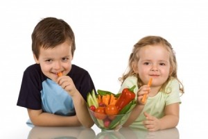 Happy kids with a bowl of vegetables, smiling and eating carrot - isolated