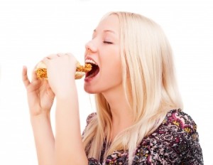 young woman eating a hamburger with chicken, isolated against white background