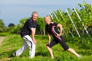 Mature or senior couple in jogging gear doing sport and physical exercise outdoors in a vineyard, stretching and gymnastics