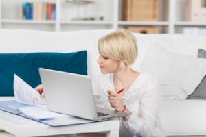 Young blond woman with file folder and laptop at home