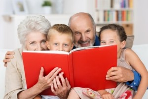 Cute little boy and girl with merry smiling eyes reading with their grandparent
