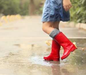 Child wearing red rain boots jumping into a puddle. Close up