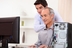 Young man teaching an elderly man computer skills