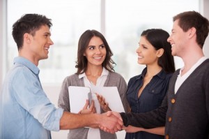 Welcome on board! Two cheerful young men handshaking while two women looking at them and smiling