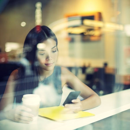 Cafe city lifestyle woman on phone drinking coffee texting text message on smartphone app sitting indoor in trendy urban cafe