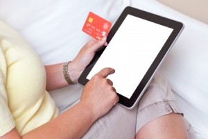 A woman sat at home making an online purchase on her tablet computer about to input her credit card details, screen is blank with a clipping path to add your own details The card is a mock up made by myself with fake details