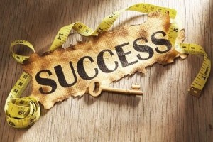 Measuring success concept using burnt paper with word success printed on it and golden key surrounded by measuring tape