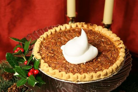 A delicious pecan pie garnished with holly and a dollop of whipped cream, photographed against a draped red silk background