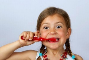 Liitle girl brushing her teeth vigorously with a red toothbrush