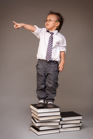 Little Chinese boy entrepreneur standing on stack of books