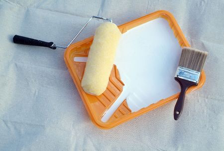 Painting supplies - paint roller and brush in orange tray liner on top of a canvas drop cloth