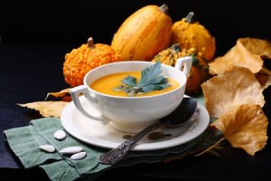 Pumpkin soup in white plate with fresh pumpkins on black background