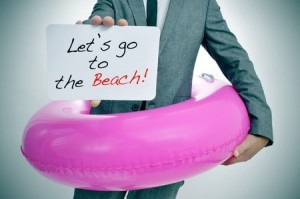 businessman with a pink swim ring showing a signboard with the text let's go to the beach written in it
