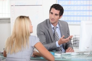 Suited man talking to a young woman across a desk