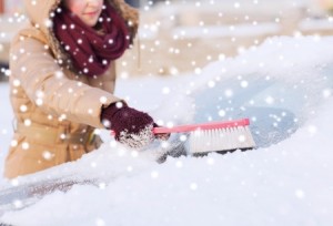 closeup of woman cleaning snow from car windshield with brush