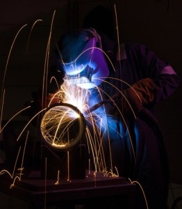 Welder uses torch to make sparks during manufacture of metal cylinder.