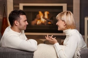 Young romantic couple sitting on sofa in front of fireplace at home