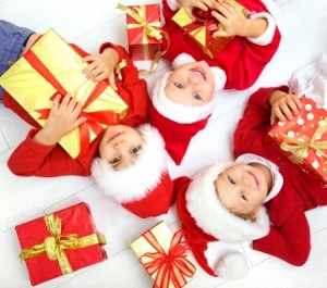 Group of 3 children in Christmas hats with presents on floor