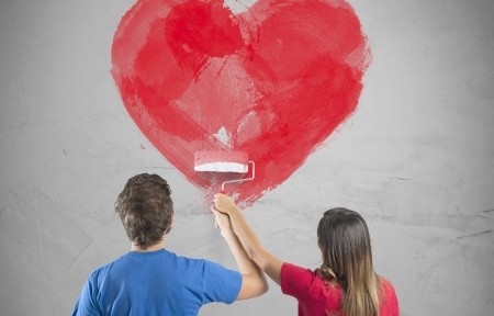 Young couple drawing a big heart in a wall