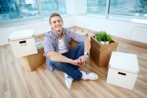 A young guy sitting on the floor of new house surrounded with boxes