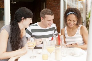 Group of young people talking together over digital tablet at coffee shop