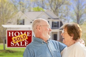 Happy Affectionate Senior Couple Hugging in Front of Sold Real Estate Sign and House.