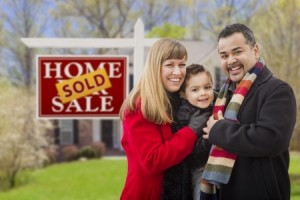 Warmly Dressed Young Mixed Race Family in Front of Sold Home For Sale Real Estate Sign and House