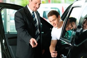 Man buying a car in dealership sitting in his new auto, the salesman talking to him and explaining details