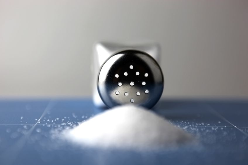 Glass saltcellar with salt on blue background