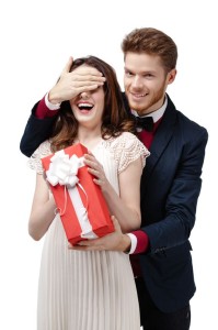 Man closes eyes of his beautiful girlfriend to give a present in red box, isolated on white