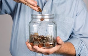 35999644 - man drops money into a glass jar for a savings account.